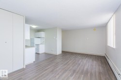 Open-concept living area featuring wood-finish flooring, white walls, and a large window with vertical blinds - 