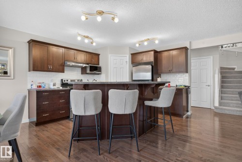 Kitchen featuring wood-finish flooring, dark wood cabinetry, a central island with bar seating, stainless steel appliances, and a white subway tile backsplash - 7858 170A Avenue, Edmonton, AB 
