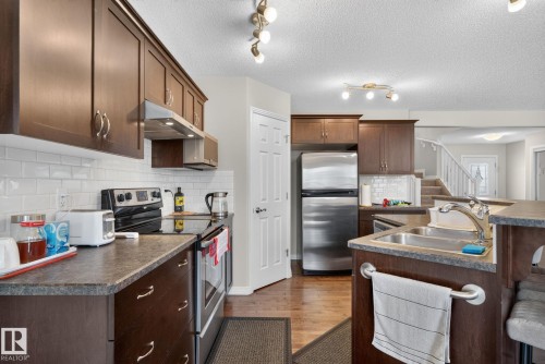 Kitchen featuring dark wood cabinetry, white subway tile backsplash, stainless steel appliances, a double basin sink, and laminate countertops - 7858 170A Avenue, Edmonton, AB 