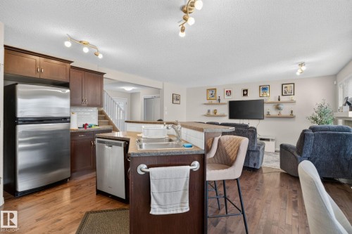 Open-concept kitchen featuring wood-finish flooring, stainless steel appliances, dark wood cabinetry, and a tiered island with integrated sink - 7858 170A Avenue, Edmonton, AB 