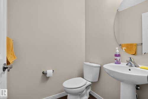Powder room featuring a pedestal sink with chrome faucet, a standard toilet, and wood-finish flooring - 7858 170A Avenue, Edmonton, AB 