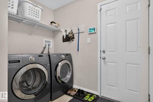 Laundry area featuring a pair of front-loading appliances, overhead wire shelving, and a paneled white door - 7858 170A Avenue, Edmonton, AB 