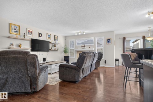 Spacious living area featuring rich wood-finish flooring, a contemporary floating shelf system, and a prominent fireplace with a mantel - 7858 170A Avenue, Edmonton, AB 