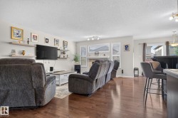 Spacious living area featuring rich wood-finish flooring, a contemporary floating shelf system, and a prominent fireplace with a mantel - 
