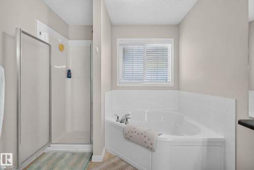 Bathroom featuring a corner soaking tub with white tile surround, a separate shower with a glass enclosure, and a window with blinds - 7858 170A Avenue, Edmonton, AB 