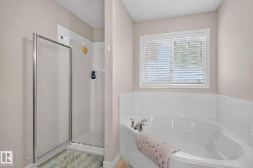 White corner soaking tub with chrome fixtures, accompanied by a separate walk-in shower with a frosted glass enclosure and a white tiled surround - 7858 170A Avenue, Edmonton, AB 