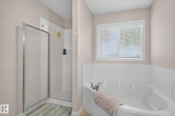 White corner soaking tub with chrome fixtures, accompanied by a separate walk-in shower with a frosted glass enclosure and a white tiled surround - 