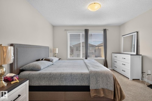 Carpeted bedroom featuring a double window with blinds and drapes, a flush-mount ceiling light, light-toned walls, and a large upholstered headboard - 7858 170A Avenue, Edmonton, AB 