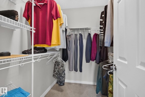 Walk-in closet featuring wire shelving, multiple hanging rods, and neutral carpeting - 7858 170A Avenue, Edmonton, AB 