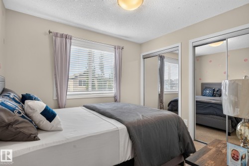 Bedroom featuring a window with horizontal blinds and curtains, two mirrored sliding closet doors, a flush-mount ceiling light, and neutral wall paint - 7858 170A Avenue, Edmonton, AB 