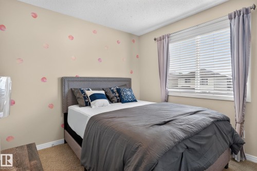 Carpeted bedroom featuring a large window with blinds and drapes, light-colored walls, and a textured ceiling - 7858 170A Avenue, Edmonton, AB 
