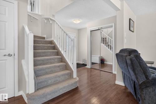 Carpeted staircase with white balusters and handrails, complemented by wood-finish flooring - 7858 170A Avenue, Edmonton, AB 