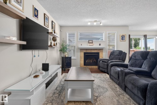 Living area featuring wood-finish flooring, a tile-surround fireplace with a mantel, and multiple windows providing natural light - 7858 170A Avenue, Edmonton, AB 