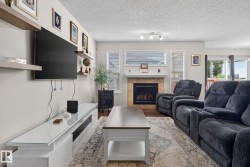 Living area featuring wood-finish flooring, a tile-surround fireplace with a mantel, and multiple windows providing natural light - 