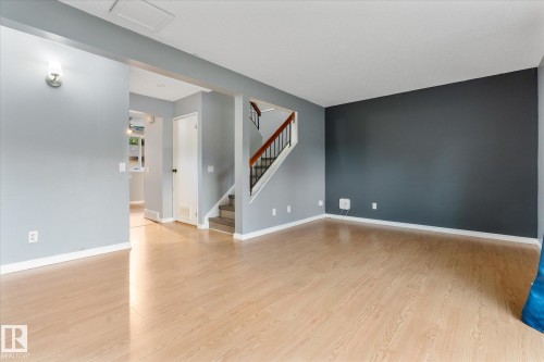 Spacious living area featuring light wood-finish flooring, a contemporary accent wall, and a staircase with wood handrails - Fort Saskatchewan, AB 