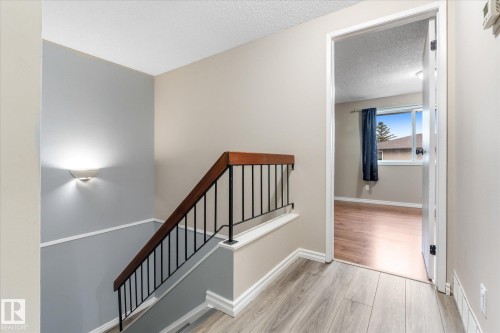 Staircase with dark wood handrail and black metal spindles, featuring a wall sconce and white baseboards - Fort Saskatchewan, AB 