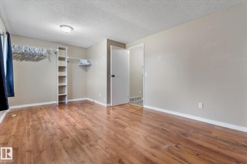 Room featuring wood-finish flooring, a built-in closet system with shelving and hanging rods, neutral wall paint, and white trim - Fort Saskatchewan, AB 
