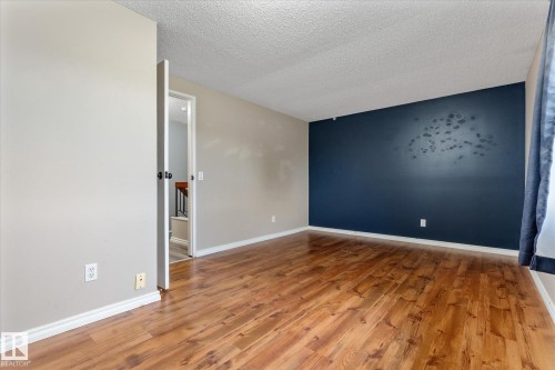 Spacious interior room featuring wood-finish flooring, a feature accent wall, light neutral wall paint, white baseboards, and a paneled door - Fort Saskatchewan, AB 