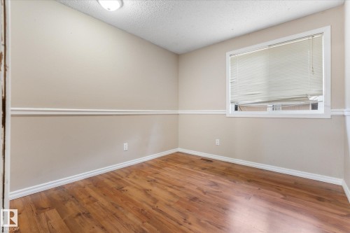 Room featuring wood-finish flooring, a contemporary ceiling light fixture, neutral-toned walls, chair rail molding, and a window with blinds - Fort Saskatchewan, AB 