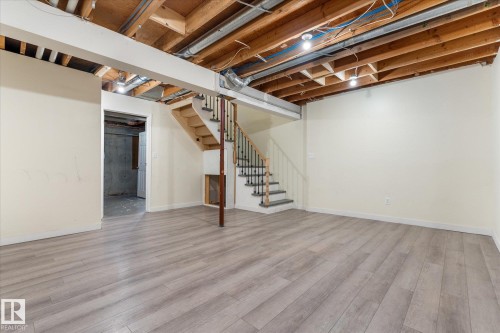 Spacious lower level featuring wood-finish flooring, light-toned walls, an exposed ceiling with structural beams, and an open staircase with black metal balusters - Fort Saskatchewan, AB 