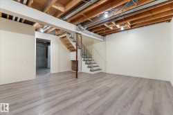Spacious lower level featuring wood-finish flooring, light-toned walls, an exposed ceiling with structural beams, and an open staircase with black metal balusters - 