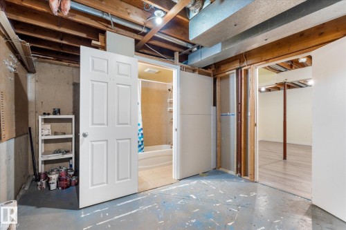 Unfinished basement featuring exposed wood joists and concrete walls, with a partial bathroom visible through an open white door - Fort Saskatchewan, AB 