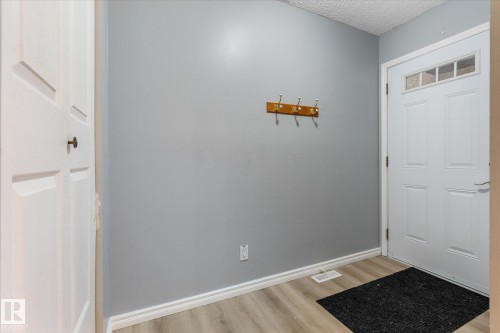 Entryway featuring light gray walls, wood-finish flooring, a white paneled door, a white front door with transom window, and white baseboards - Fort Saskatchewan, AB 