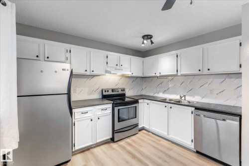 Contemporary kitchen featuring white cabinetry, stainless steel appliances, dark countertops, and a patterned backsplash - Fort Saskatchewan, AB 