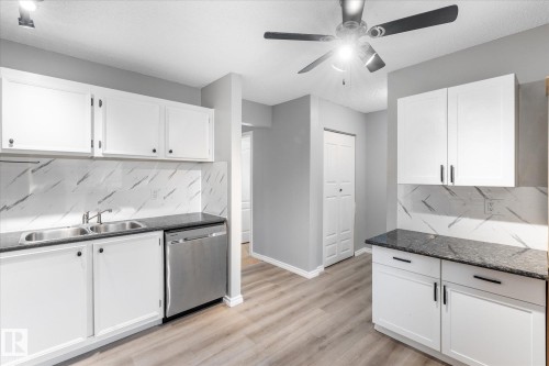 Kitchen featuring white cabinetry, dark stone-finish countertops, stainless steel sink, and stainless steel dishwasher - Fort Saskatchewan, AB 