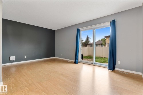 Spacious room featuring light wood-finish flooring and a sliding glass patio door - Fort Saskatchewan, AB 