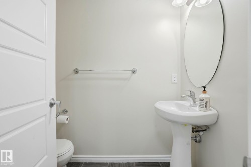 Pedestal sink with chrome faucet, complemented by a large oval mirror and a two-light vanity fixture - 445 Watt Boulevard, Edmonton, AB 