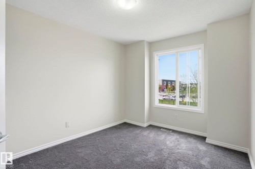 Bright room featuring a large window, neutral wall paint, white trim, and dark carpet flooring - 445 Watt Boulevard, Edmonton, AB 