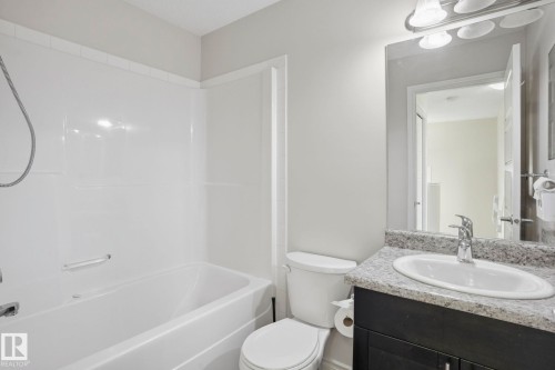 Bathroom featuring a white bathtub with a shower surround, a toilet, a vanity with a grey speckled countertop, an undermount sink, and a framed mirror with overhead lighting - 445 Watt Boulevard, Edmonton, AB 