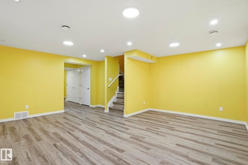 Spacious room featuring wood-finish flooring, recessed lighting, bright yellow walls, white baseboards, and a visible staircase with white railing - 445 Watt Boulevard, Edmonton, AB 
