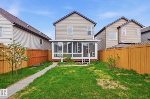 Rear exterior with a sunroom, expansive yard, concrete pathway, and wood fencing - 445 Watt Boulevard, Edmonton, AB 