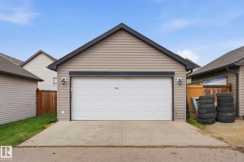 Detached garage featuring horizontal siding, a gabled roofline with dark trim, a paneled overhead door, and two exterior wall sconces - 445 Watt Boulevard, Edmonton, AB 