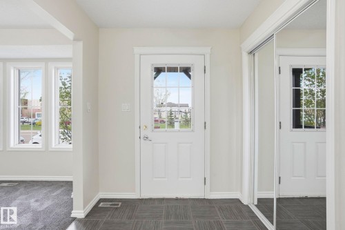 Entryway with dark tile flooring, white paneled door featuring multiple glass panes, and a mirrored closet door - 445 Watt Boulevard, Edmonton, AB 