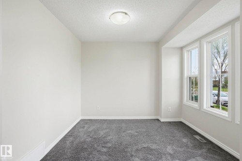 Bright interior space featuring a trio of large windows with white trim, gray wall-to-wall carpeting, light neutral wall paint, and a flush-mount ceiling light fixture - 445 Watt Boulevard, Edmonton, AB 
