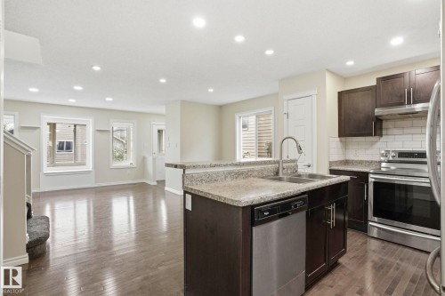 Open-concept kitchen featuring dark wood cabinetry, stainless steel appliances, a subway tile backsplash, and a breakfast bar with an undermount sink - 445 Watt Boulevard, Edmonton, AB 