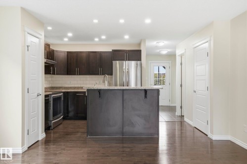 Kitchen featuring dark wood cabinetry, stainless steel appliances, a center island with countertop, and subway tile backsplash - 445 Watt Boulevard, Edmonton, AB 