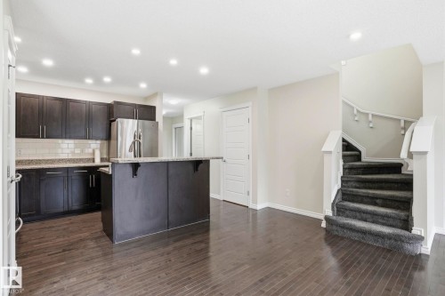 Modern kitchen featuring dark wood cabinetry, stainless steel appliances, a center island with a breakfast bar, and white subway tile backsplash - 445 Watt Boulevard, Edmonton, AB 