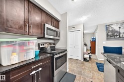 Kitchen featuring dark wood cabinetry, stainless steel appliances including a microwave and range, dark stone countertops, and square floor tiles - 