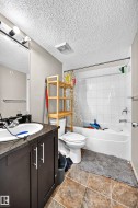 Bathroom featuring a built-in vanity with a dark countertop and white basin, a white toilet, and a white bathtub with subway tile surround - 