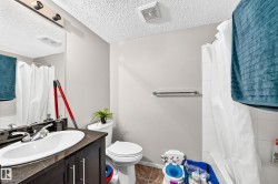 Bathroom featuring a vanity with an integrated sink, dark wood-finish cabinetry, a toilet, a shower with white subway tile, and a textured ceiling - 