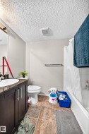 Bathroom featuring a dark wood-finish vanity with an undermount sink, a toilet, an integrated bathtub and shower with white subway tile surround, and square tile flooring - 