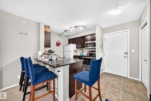 Kitchen featuring dark wood cabinetry, stainless steel appliances, and a breakfast bar with a dark countertop - 417 1510 Watt Drive, Edmonton, AB 