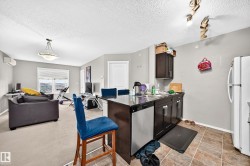 Open-concept living area featuring a kitchen island with dark wood-finish cabinetry, stainless steel dishwasher, and a white refrigerator - 