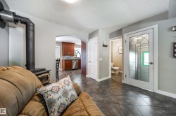 Living area featuring a black wood stove with metal chimney, dark tile flooring, and an arched doorway leading to a kitchen with wood cabinetry and stainless steel appliances - 