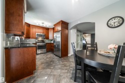 Open concept kitchen and dining area featuring rich wood cabinetry, stainless steel appliances, dark granite countertops, and a subway tile backsplash - 