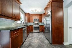 U-shaped kitchen featuring wood cabinetry, stainless steel appliances, dark countertops, a light subway tile backsplash, and patterned tile flooring - 